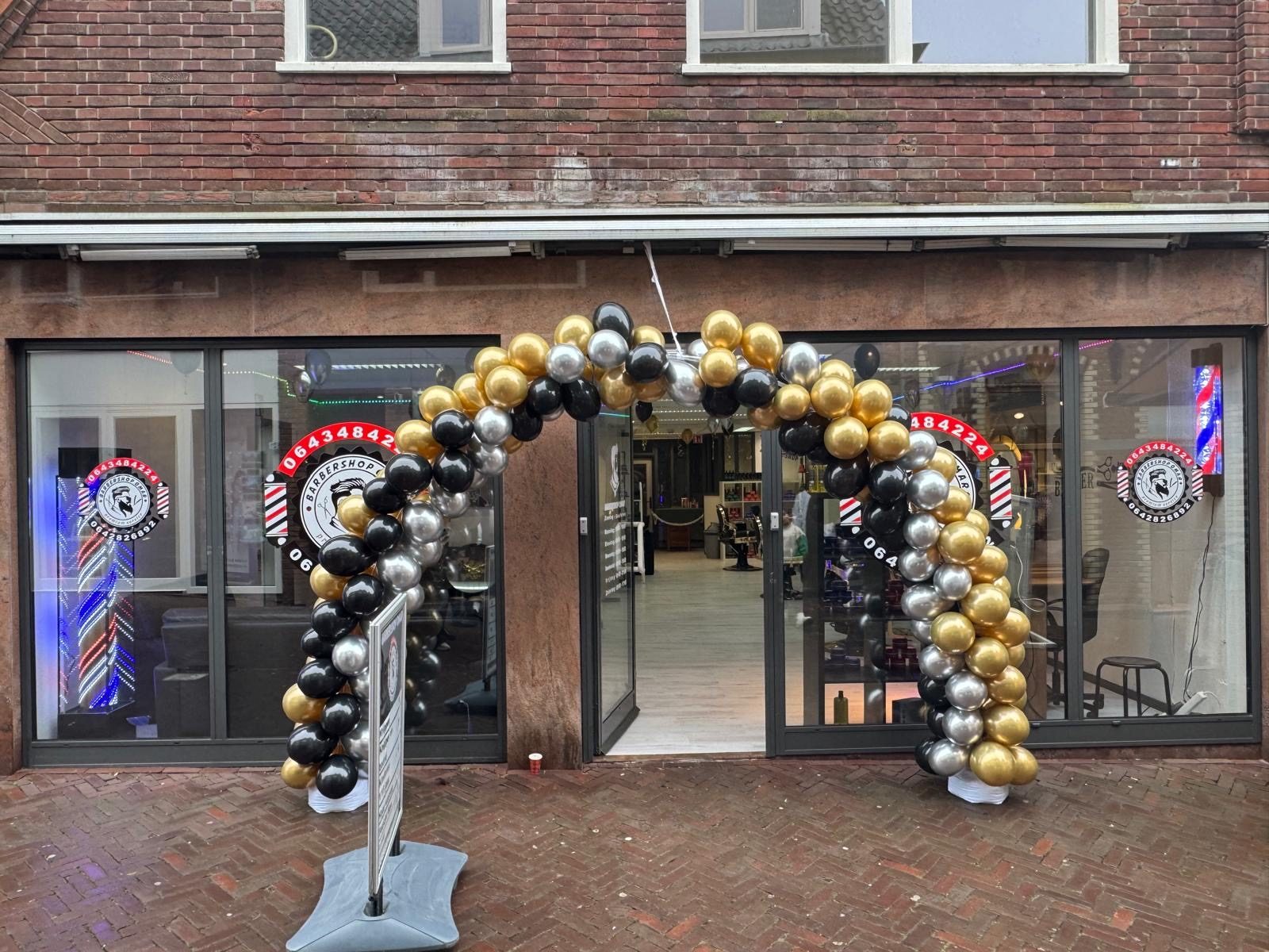De gevel van de zaak met een ballonnenboog in zwart, goud en zilver bij de opening