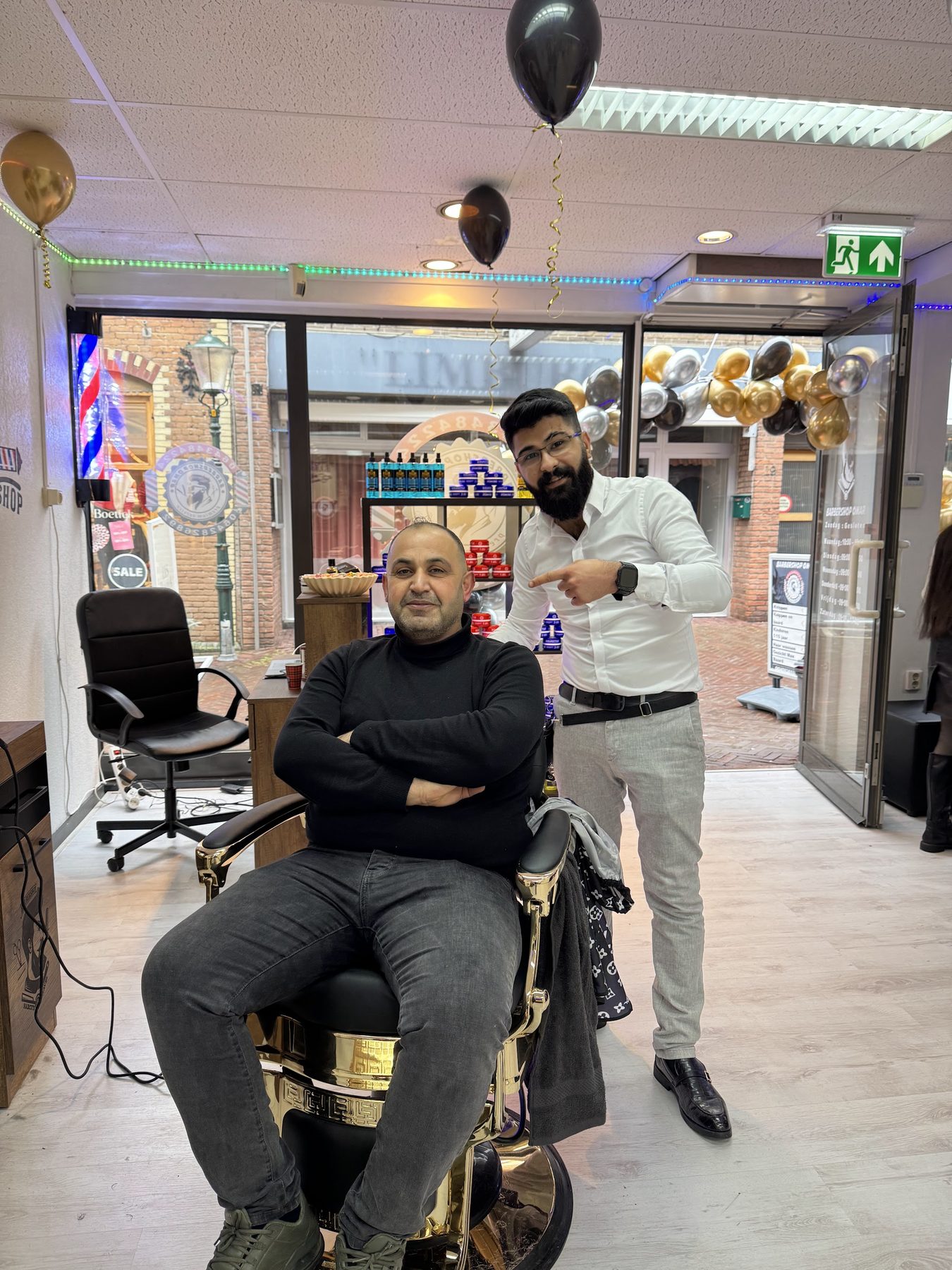Klant en barbier bij de gouden stoel, met de ingang van de zaak op de achtergrond